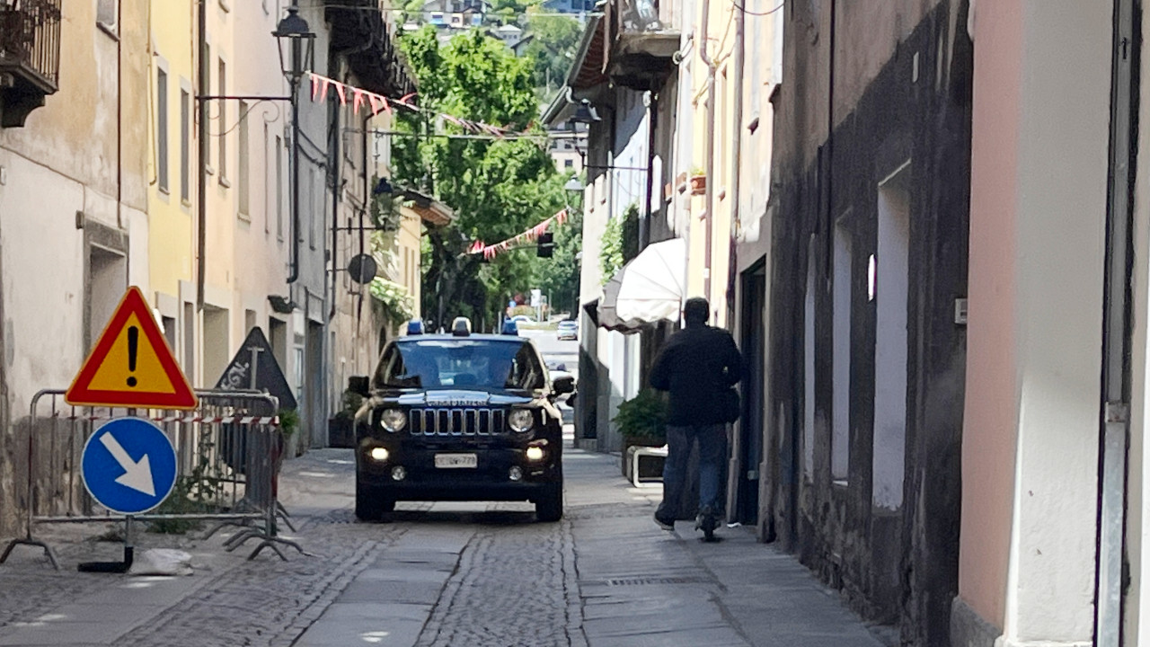 Nel centro storico di Aosta una persona in monopattino, senza casco, passa a fianco di un'auto dei Carabinieri